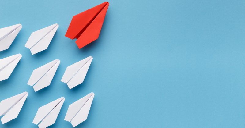Red paper airplane going upwards and leading other paper airplanes